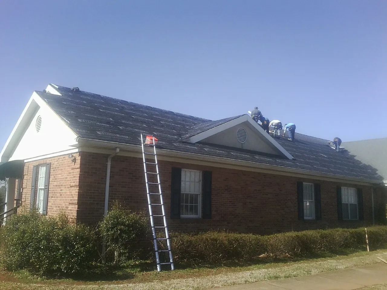 Crew tearing shingles off a brick ranch roof with a ladder set — Metal Roof Repair work by our crew in Ivor