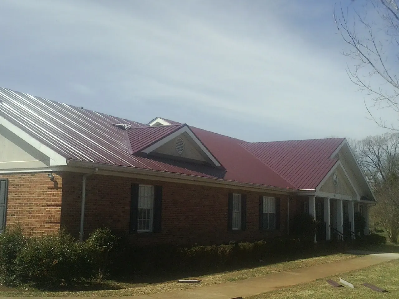 Red metal roof with gabled entries on a long brick building, from a Hail Damage Roof Repair job in Ivor