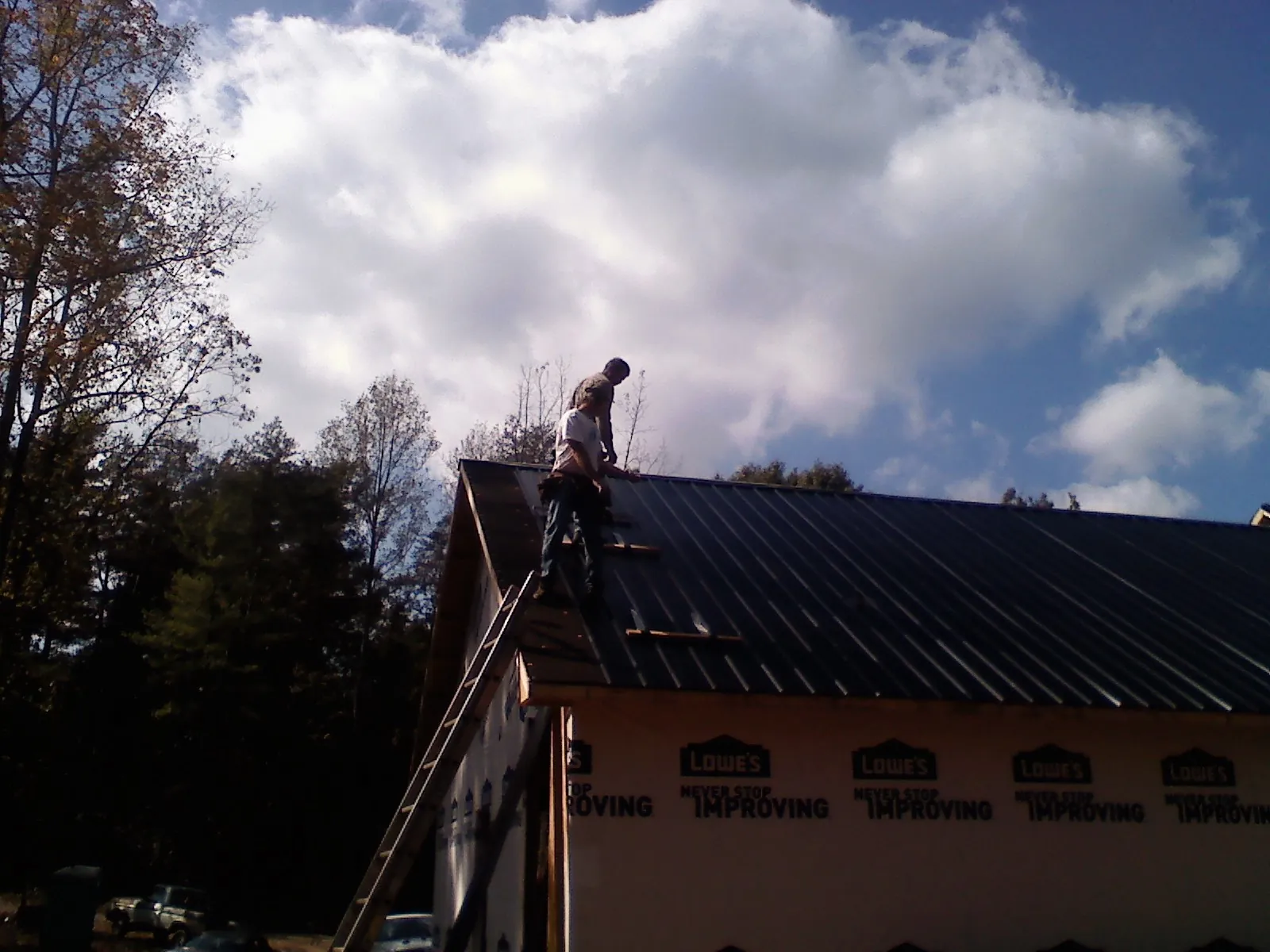 Roofer fastening dark metal panels high against a cloudy sky, from a Roof Inspection job in Ivor