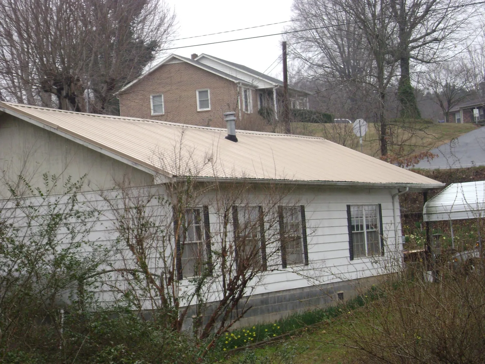 Tan metal roof on a white sided house set into a hillside — Commercial Roofing by Roofing Brothers in Ivor